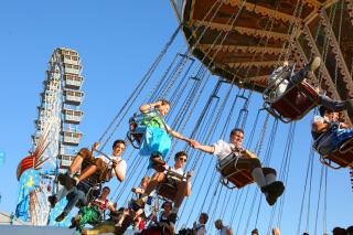 Menschen auf Kettenflieger, Riesenrad im Hintergrund, Oide Wiesn, blauer Himmel