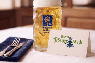 Auf dem Bild ist ein Tisch zu sehen, auf dem ein gefüllter Augustinerbierkrug, ein Gedeck und ein Reservierungsschild mit der Aufschrift Bartls Flösserstadl sind.