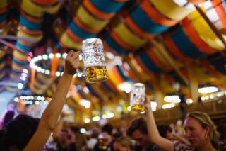 Feiernde Menschen halten einen Maßkrug in einem Festzelt in die Luft