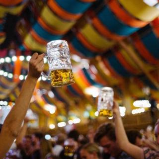 Feiernde Menschen halten einen Maßkrug in einem Festzelt in die Luft